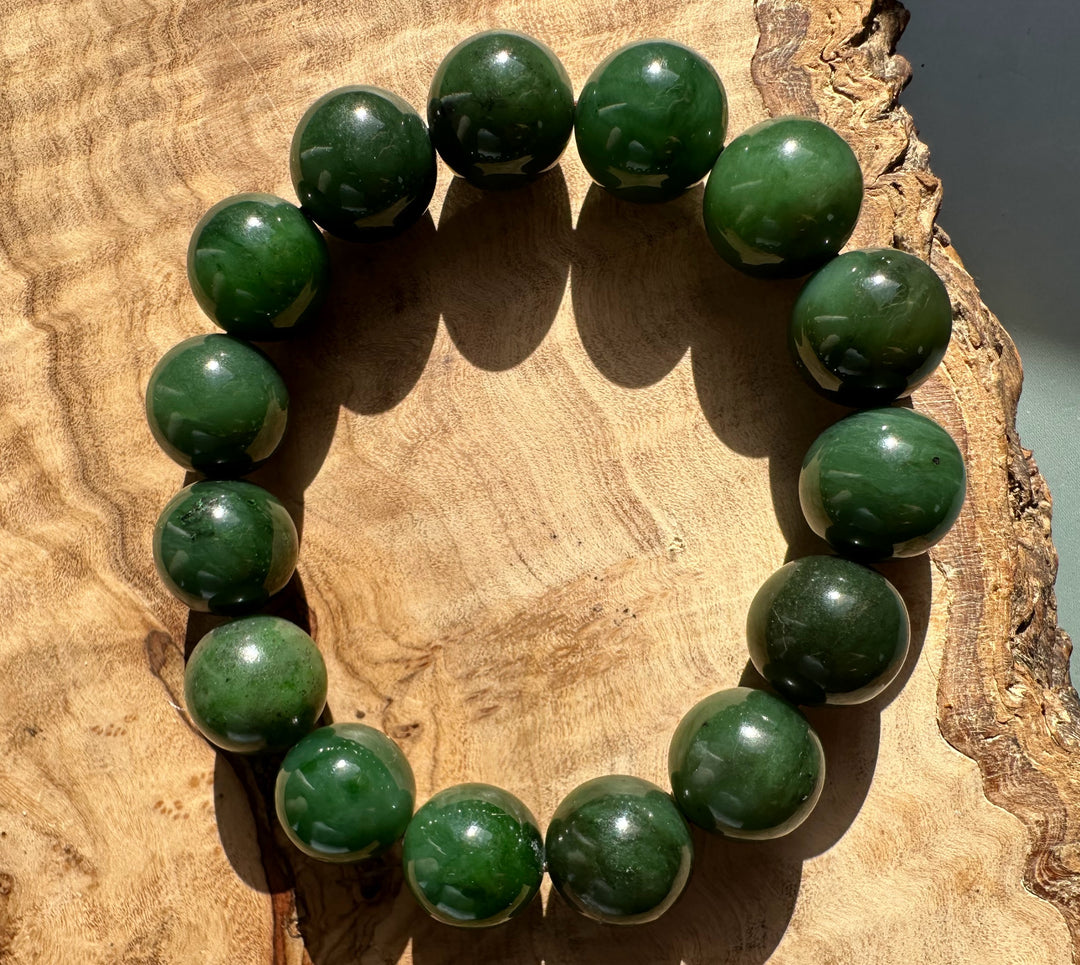 Circular strand of 14mm nephrite jade beads forming a bracelet on a sunlit wooden surface.