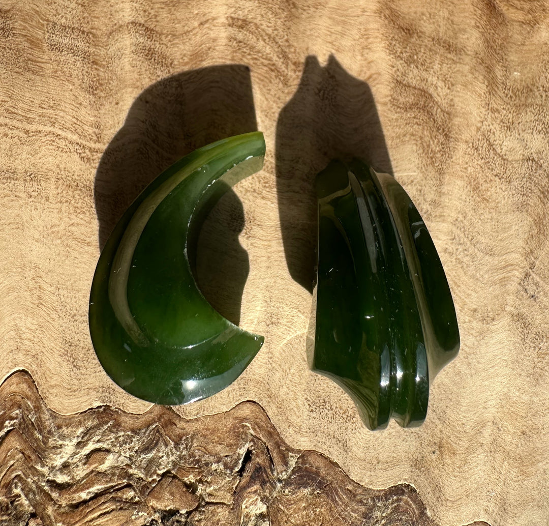 Two dark green jade crescent earring pieces on a wood surface