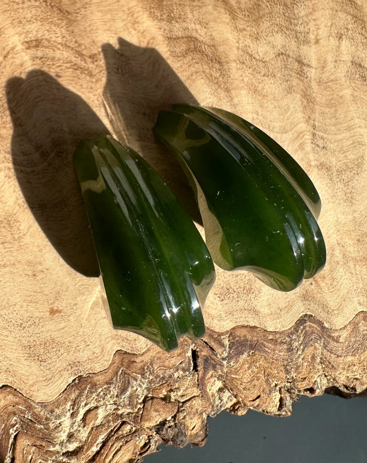 Pair of dark green carved jade earrings on a wood surface