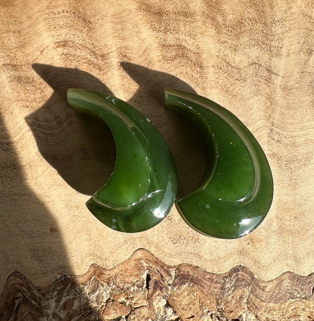 Canandian Jade carved crescent earrings not set resting on a textured wooden surface