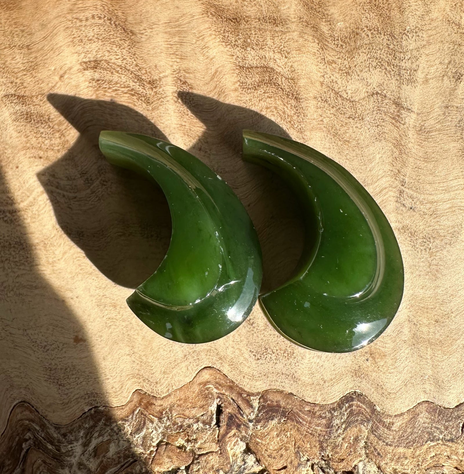 Canandian Jade carved crescent earrings not set resting on a textured wooden surface