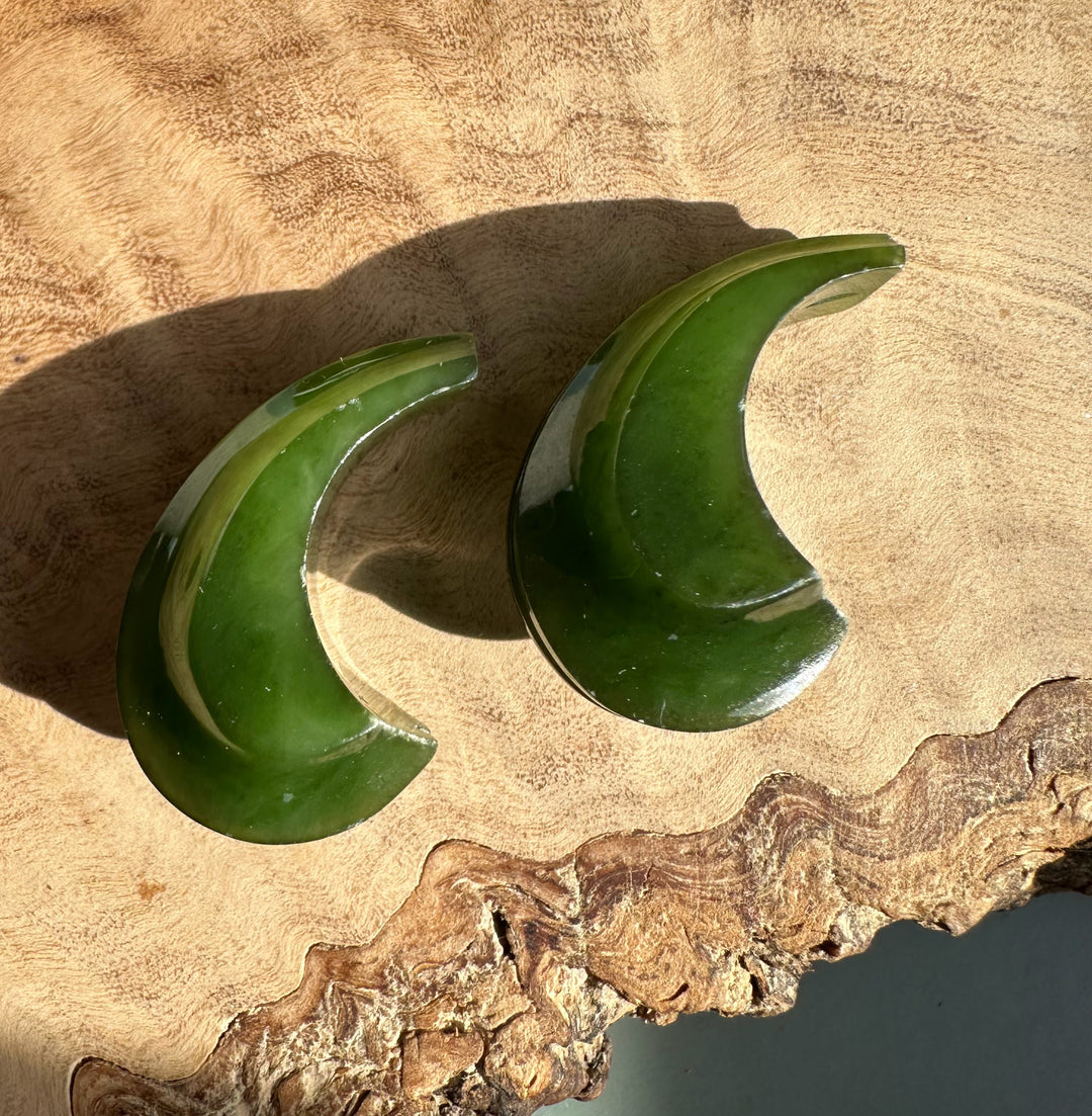 Canandian jade carved crescent earrings not set two glossy green crescents on wood surface