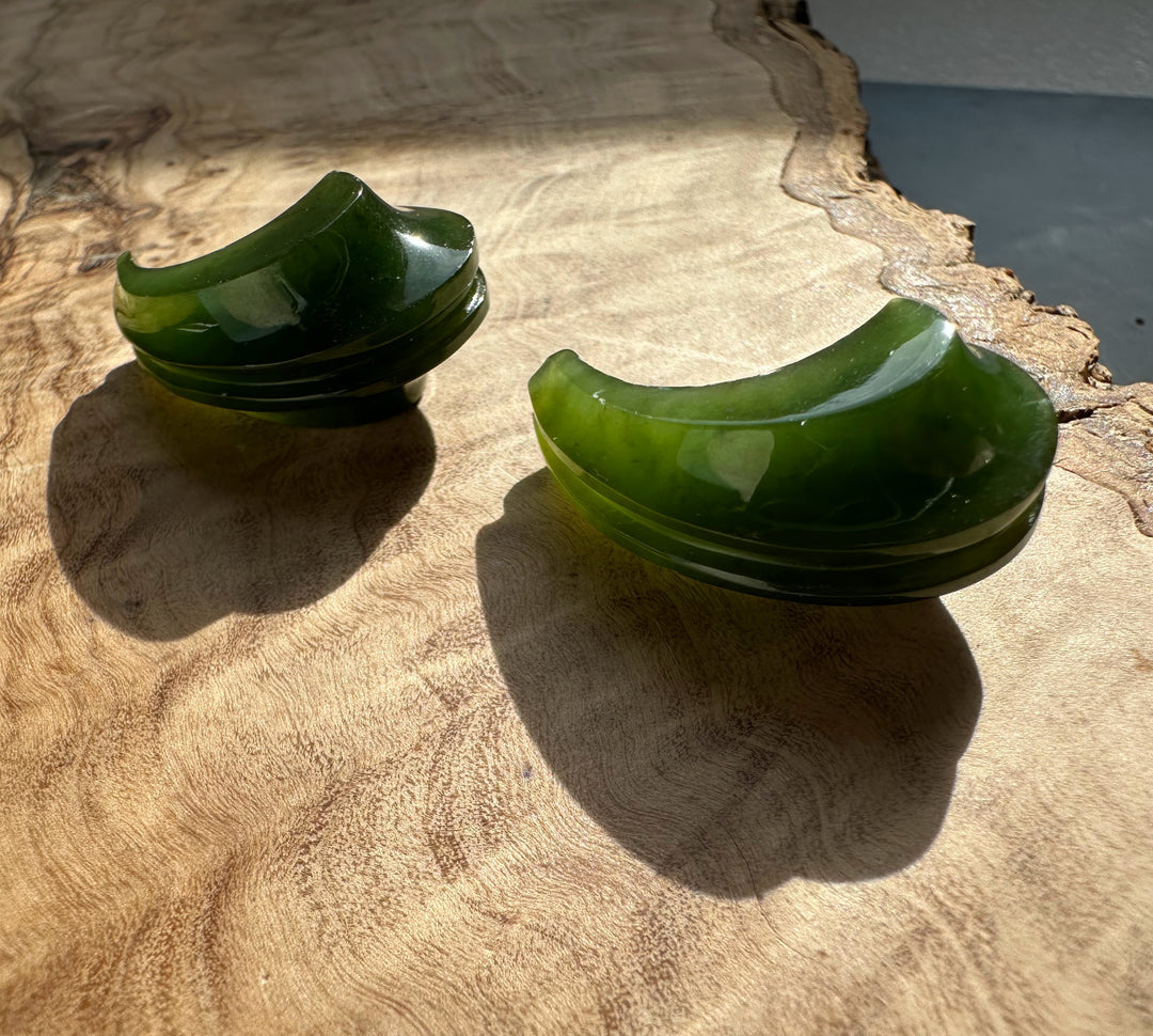 Canadian jade carved crescent earrings stacked on a rustic wood surface