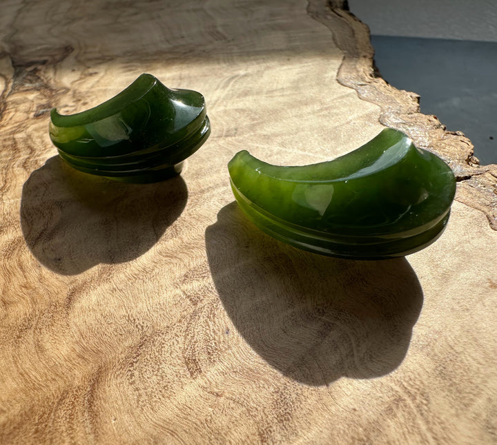 Canadian jade carved crescent earrings stacked on a rustic wood surface