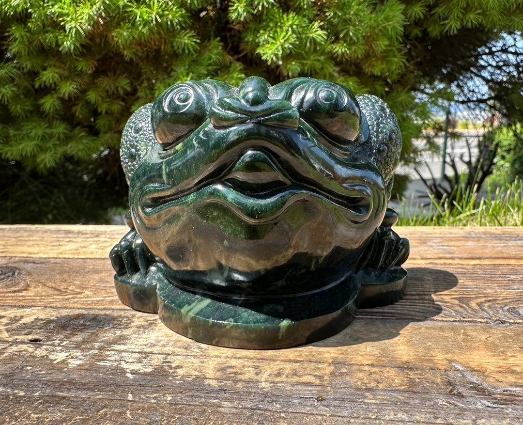 Front view of the dark green Ogden Jade Toad statue on a weathered wooden surface outdoors.