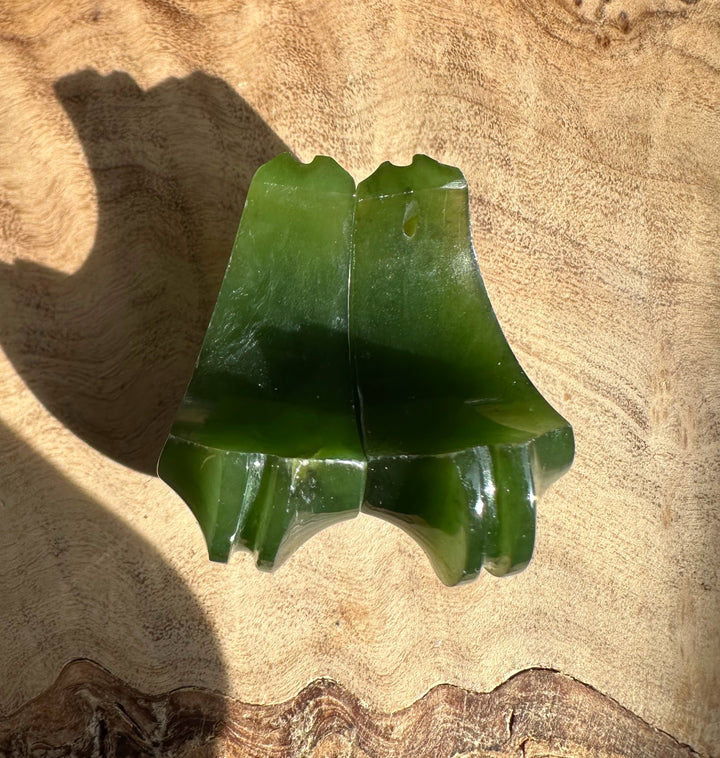 Pair of green jade carved crescent earrings lying on wood background.