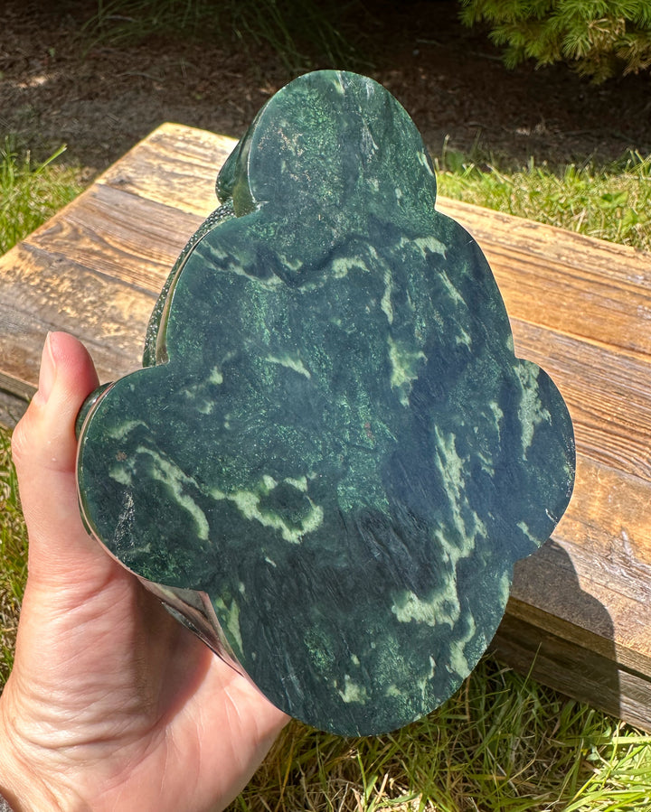 Hand holds four lobed dark green jade toad sculpture with marbled patterns.