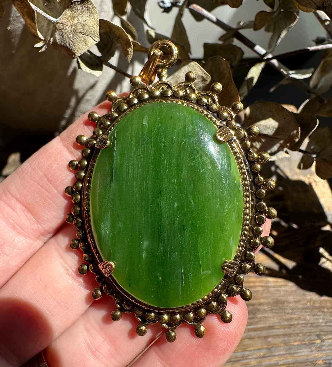 Large oval green jade pendant set in an ornate gold bezel with a beaded border
