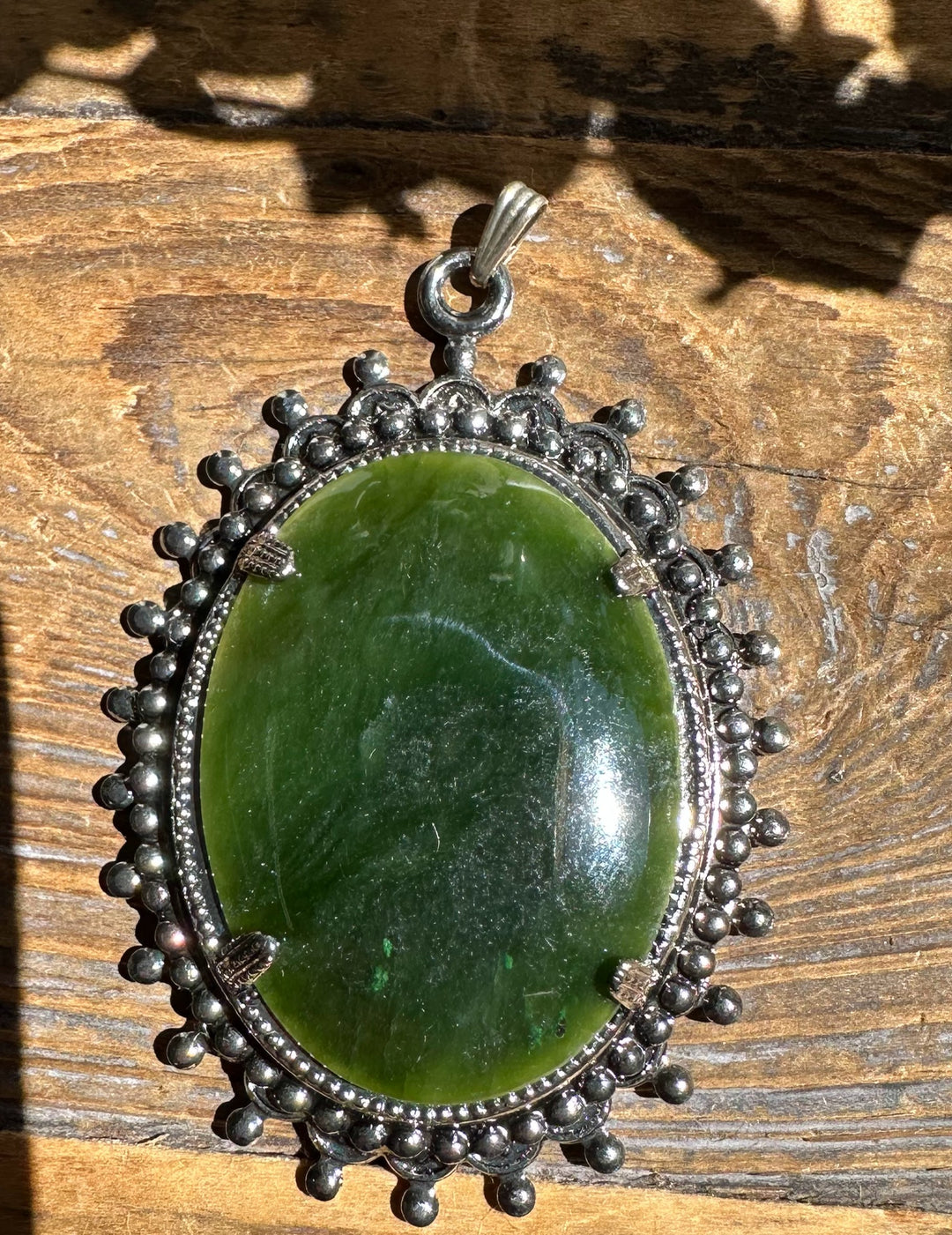 Close up of large green jade oval pendant in an ornate antique silver bezel with beaded rim