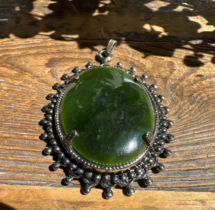 Large vintage jade oval pendant with a silver beaded surround and bail on a wooden surface