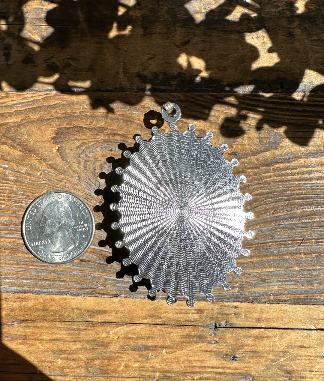 Back of the pendant with a silver radiating sunburst pattern and a hanging bail at the top.