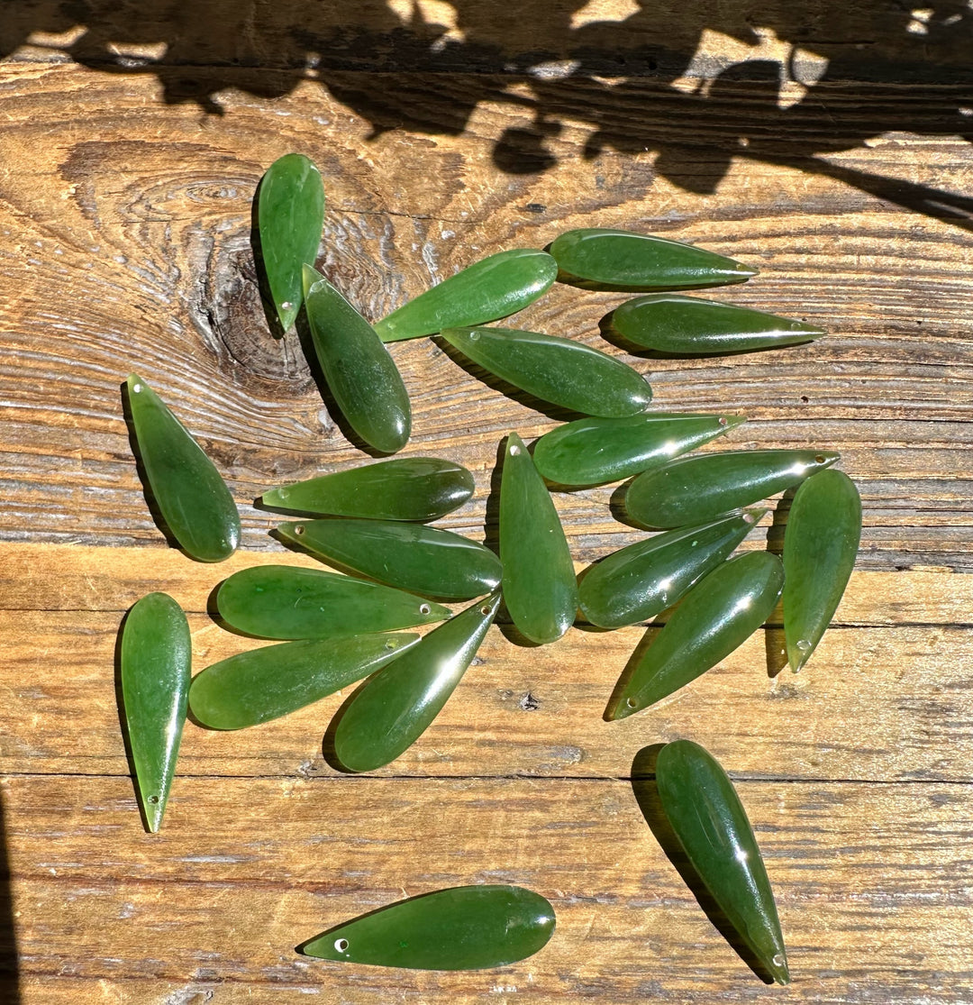Nephrite jade teardrop pieces with drilled holes scattered on a wooden surface