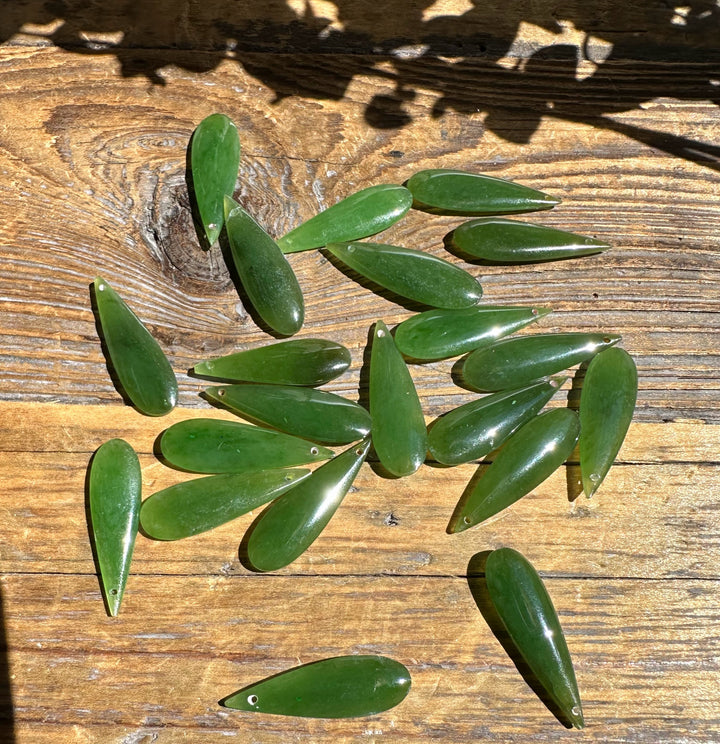 Nephrite jade teardrop pieces with drilled holes scattered on a wooden surface