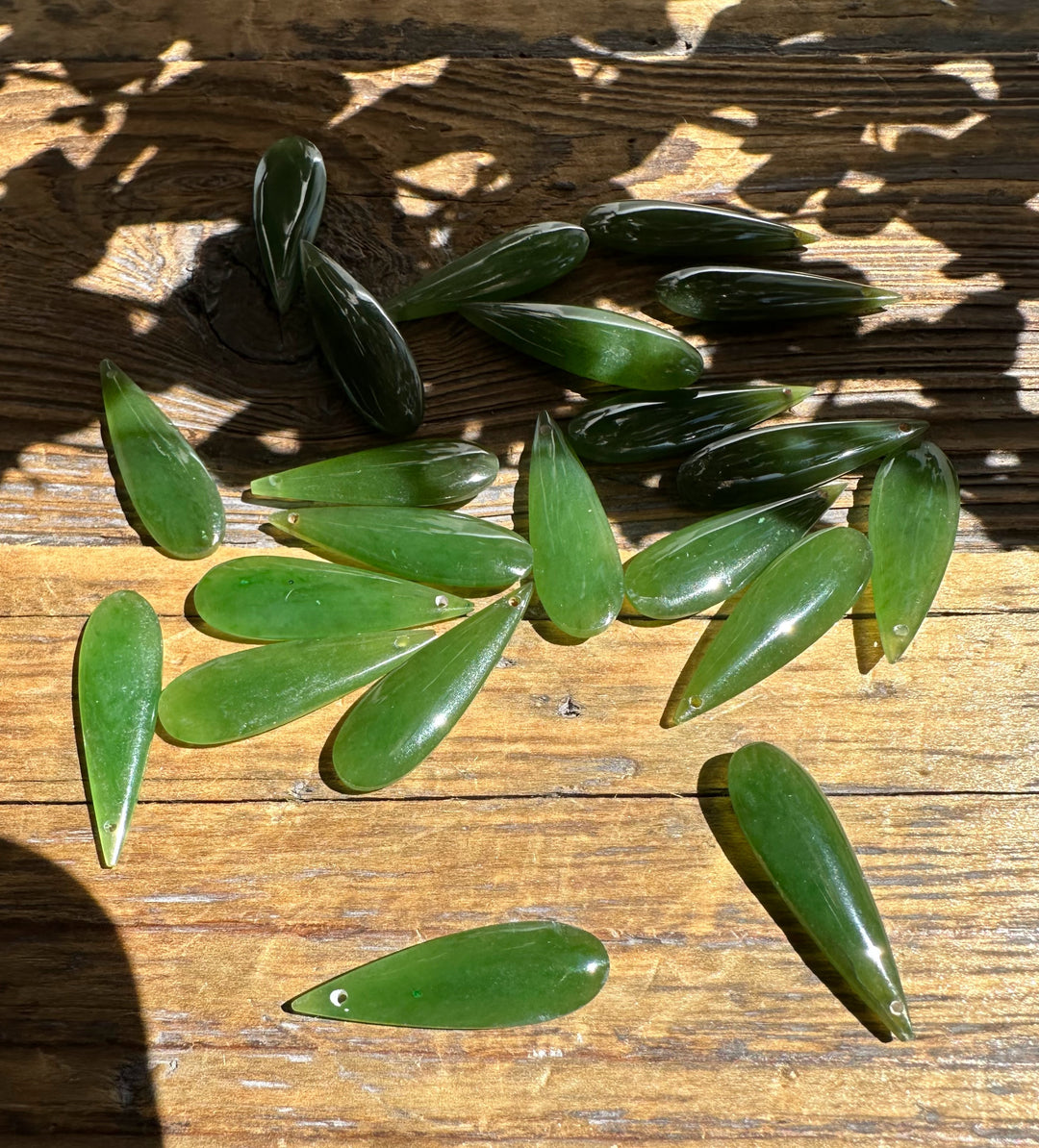 A Grade Canadian nephrite jade teardrop pieces arranged on a weathered wooden surface