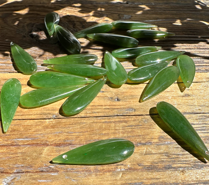 A Grade Canadian nephrite jade teardrops scattered on a weathered wooden surface