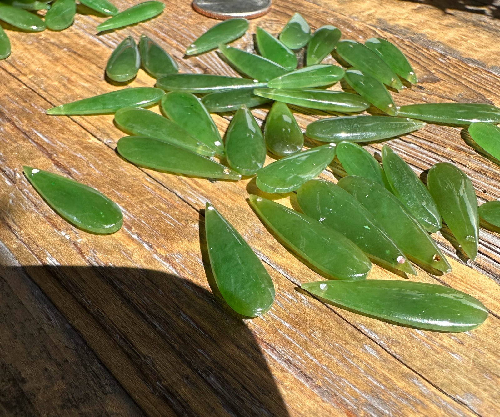 A Grade Canadian nephrite jade teardrops on wood with a coin for scale