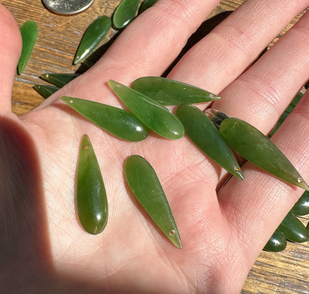 Hand holds several green nephrite jade teardrops with drilled holes for jewelry