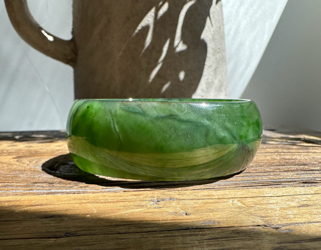 A Grade Ogden Jade Bangle in vibrant green with lighter swirls, set on a weathered wooden surface.