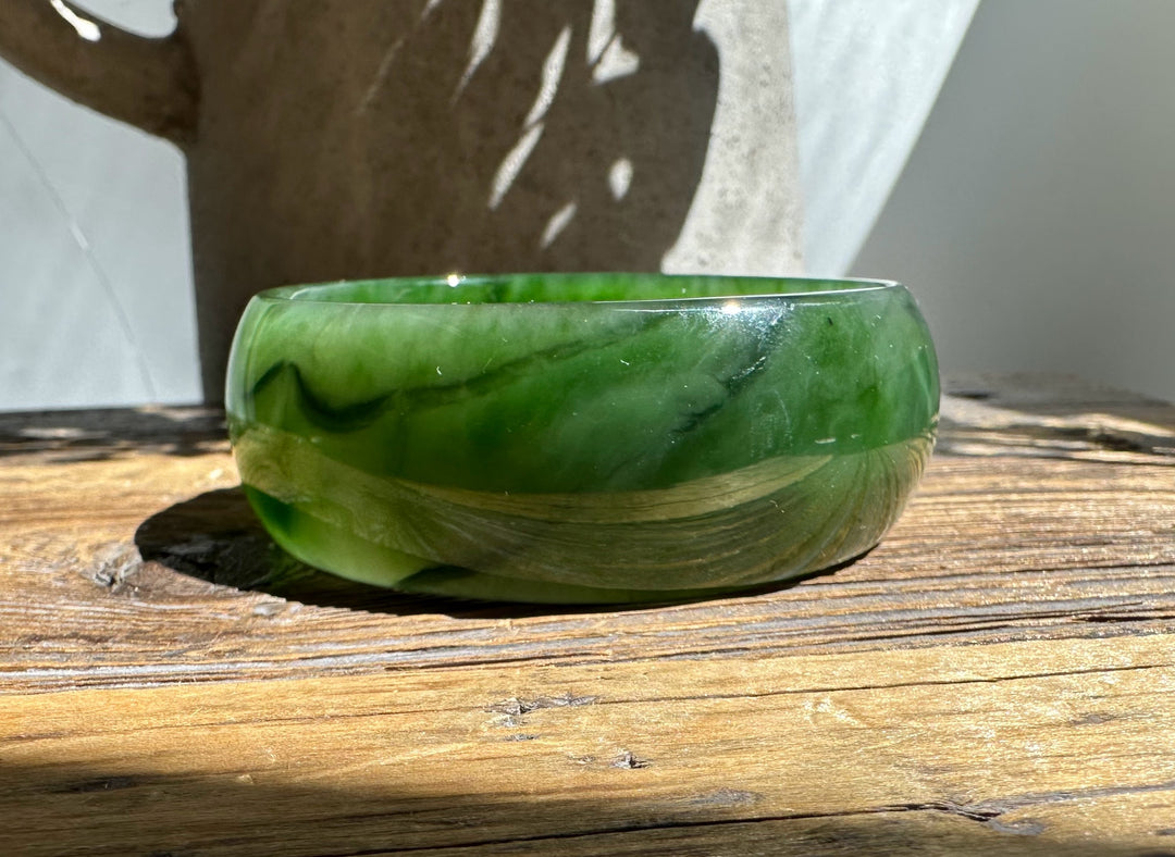 Green jade bangle resting on a wooden surface in bright sunlight, with sweeping natural veins.