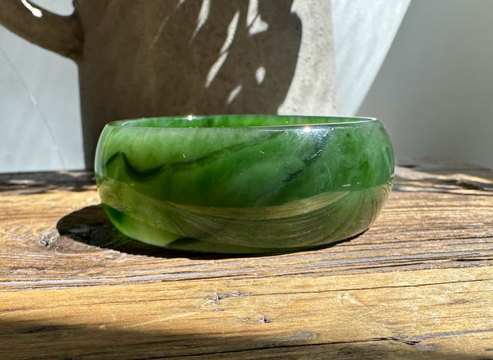 Green jade bangle resting on a wooden surface in bright sunlight, with sweeping natural veins.