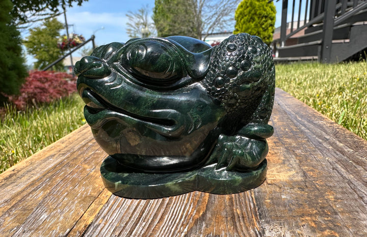 Dark green Ogden jade toad sculpture resting on a weathered wooden table outdoors
