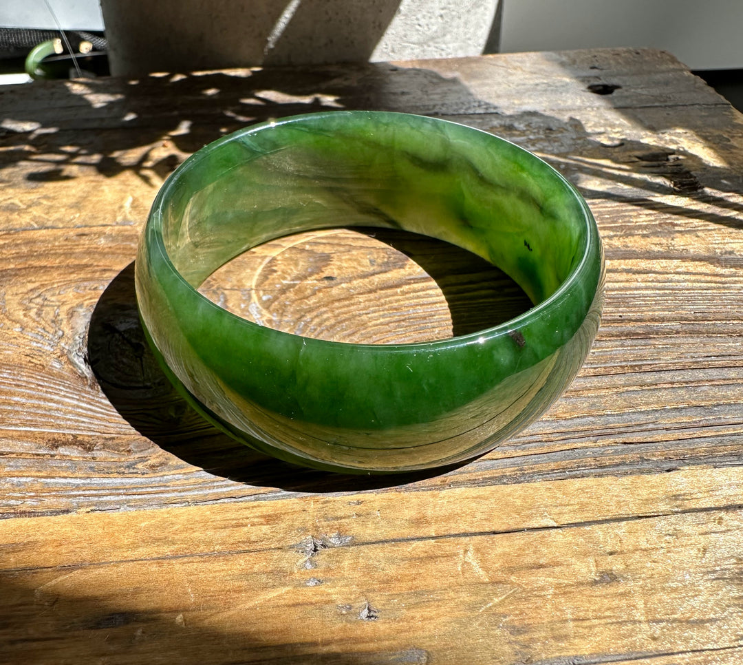 A Grade Ogden jade bangle in bright green rests on a weathered wooden surface in sunlight
