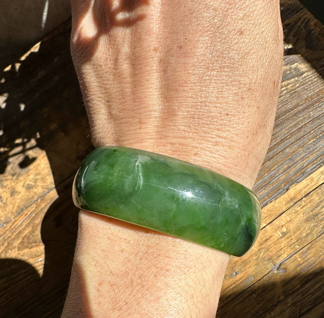 Side view of Ogden jade bangle on wrist, smooth glossy green surface.