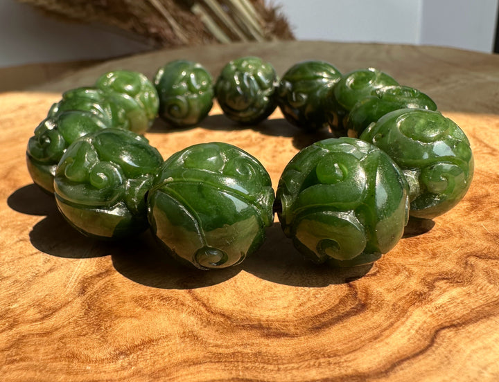 A green carved stone jade bracelet arranged in a circle on a wooden surface, with carved details visible on each bead.