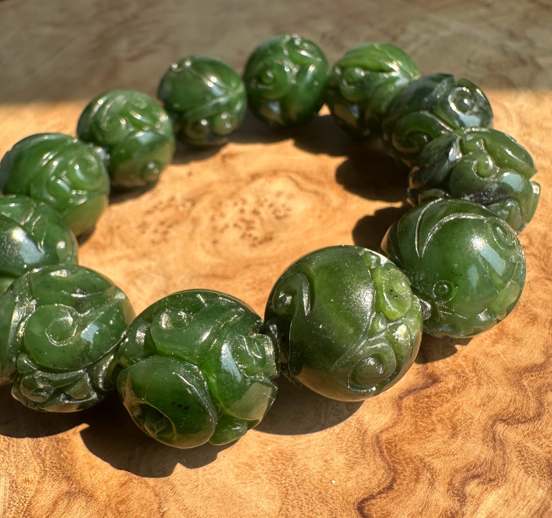A beaded bracelet made of carved green jade beads, arranged in a circle on a textured wooden surface.