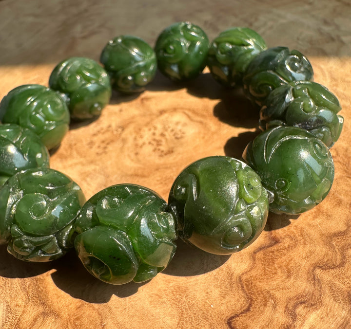 A beaded bracelet made of carved green jade beads, arranged in a circle on a textured wooden surface.