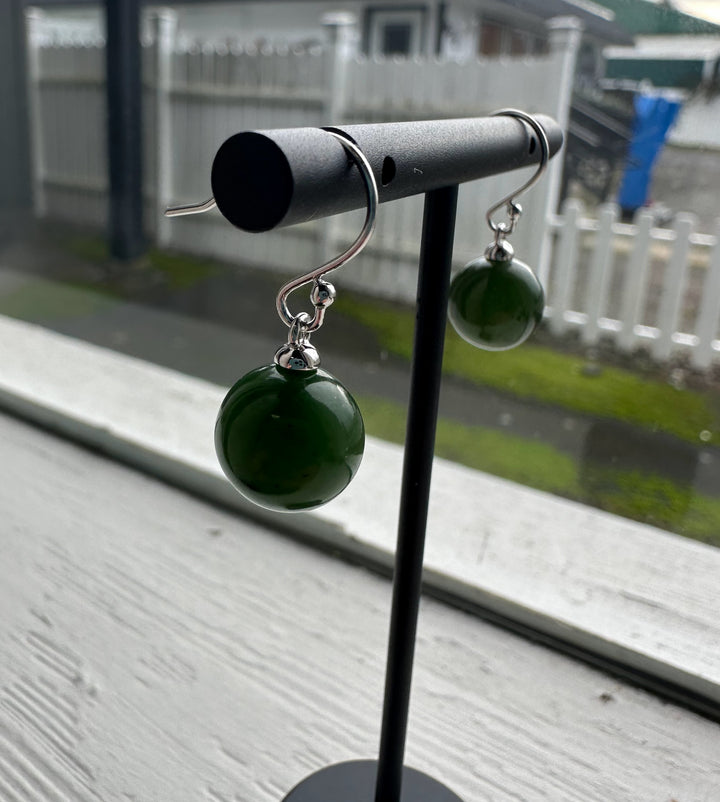 Canadian Jade Earrings with large green jade beads hanging from silver hooks displayed on a stand by a window