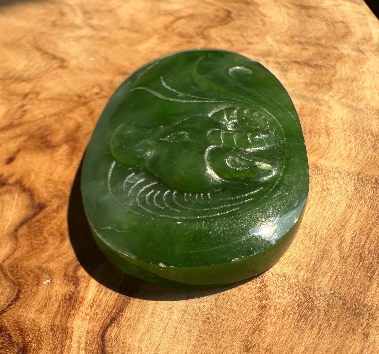 A polished green jade pendant with a carved buffalo motif, resting on a textured wooden surface.