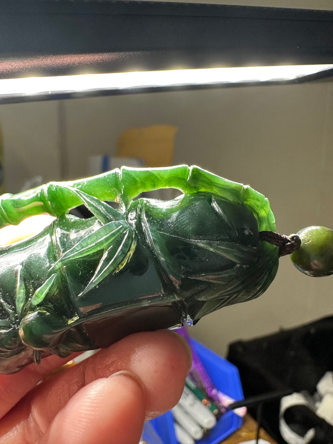 Handheld close up of the jade spider pendant showing carved bamboo details and a cord bead.
