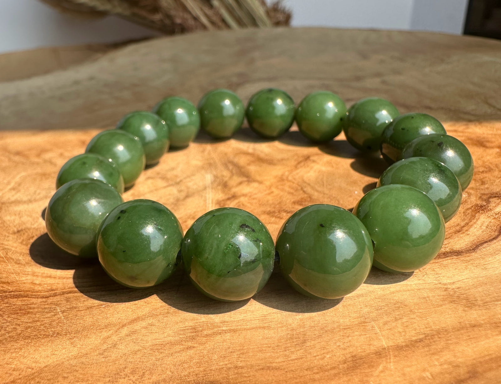 A beaded bracelet made of glossy green jade beads, arranged in a circle on a warm-toned wooden surface.