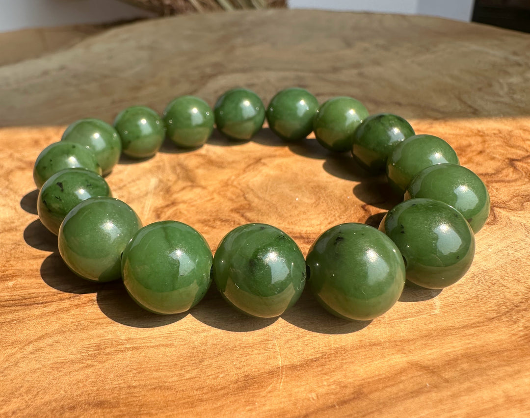 A beaded bracelet made of glossy green jade beads arranged in a circle on a wooden surface.