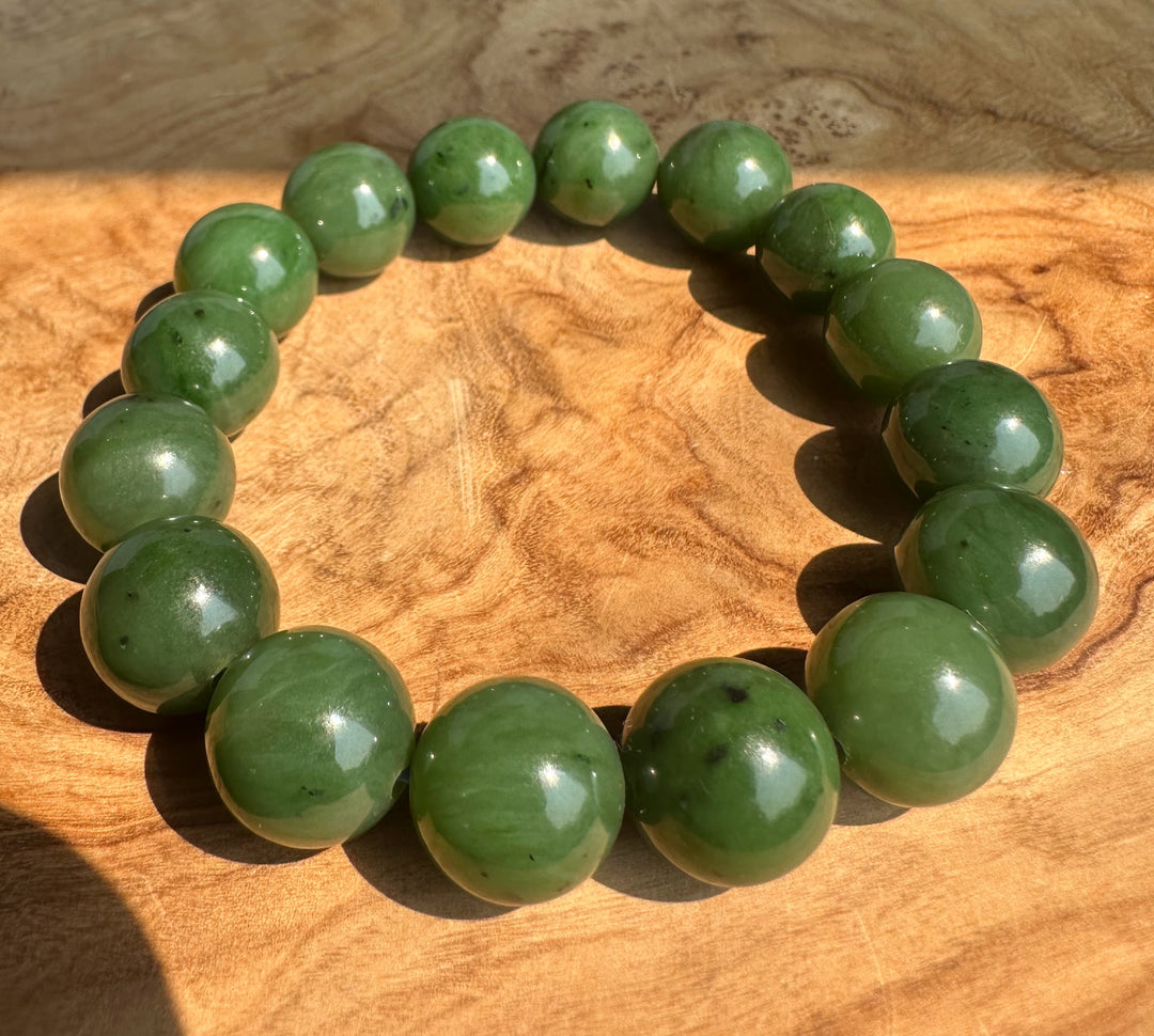 A beaded stretch bracelet made of polished green jade round beads, displayed on a textured wooden surface.