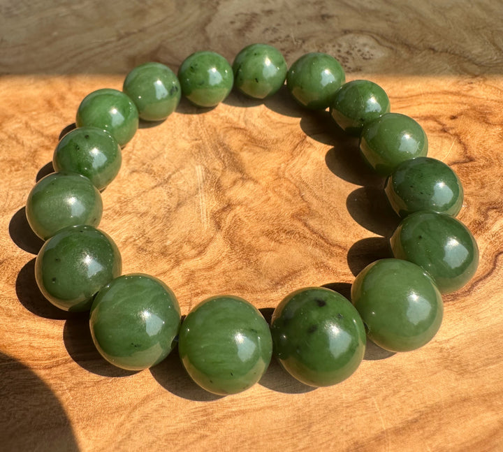 A beaded stretch bracelet made of polished green jade round beads, displayed on a textured wooden surface.