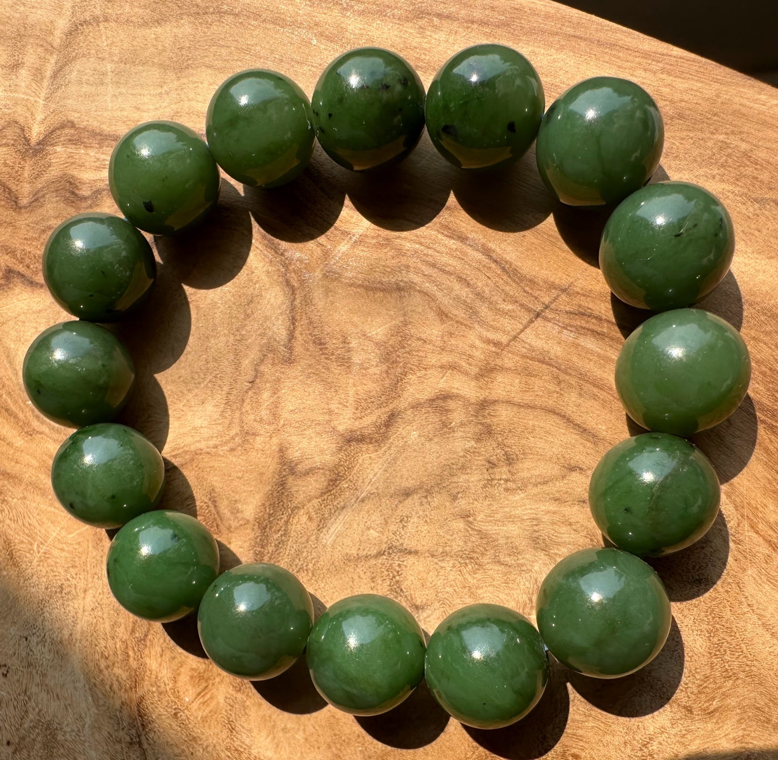 A beaded bracelet made of jade green polished round beads, arranged in a circle on a textured wooden surface.