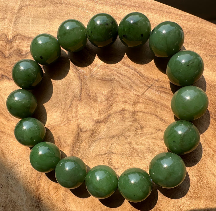 A beaded bracelet made of jade green polished round beads, arranged in a circle on a textured wooden surface.