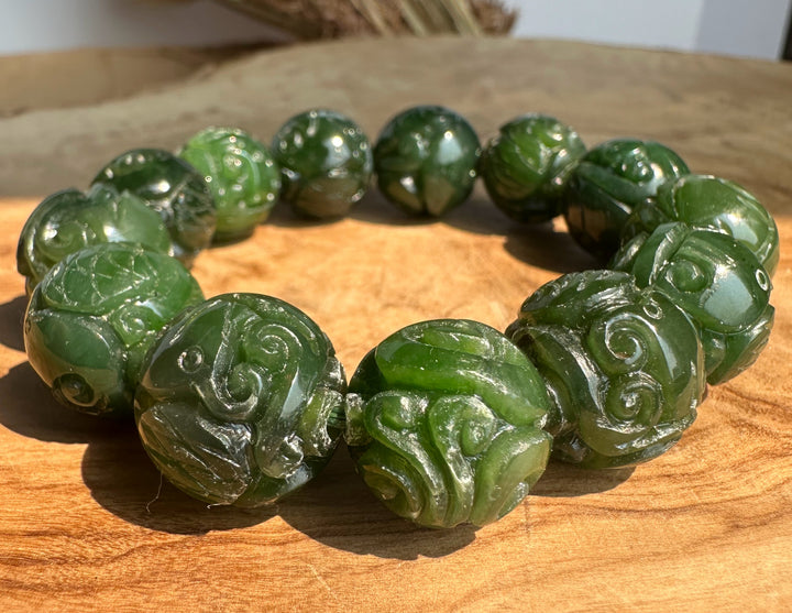 Side view of a nephrite jade bracelet with 16mm carved beads on a wood tabletop