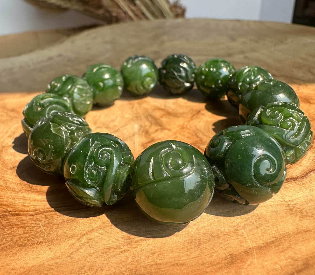 Close up of glossy carved nephrite jade beads forming a bracelet on a wood surface