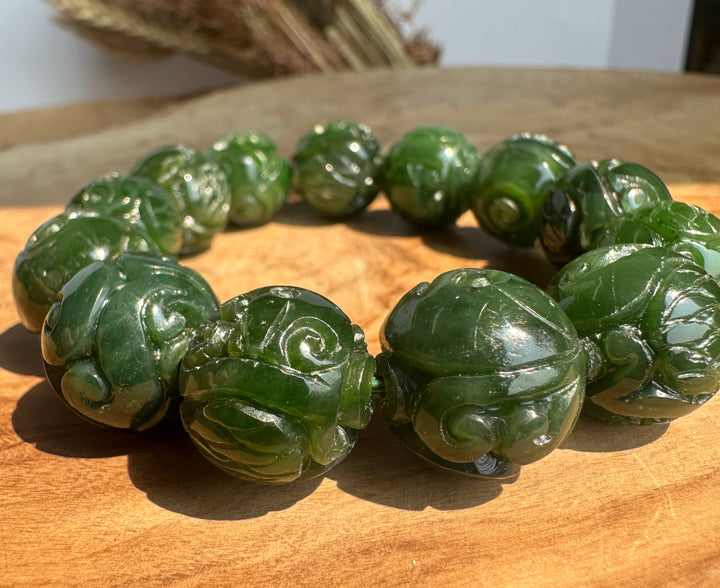 Nephrite jade bracelet with 16mm carved round beads resting on a wooden surface