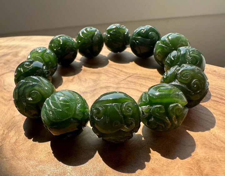 Nephrite jade 16mm carved beads forming a circular bracelet viewed from above on a wooden surface