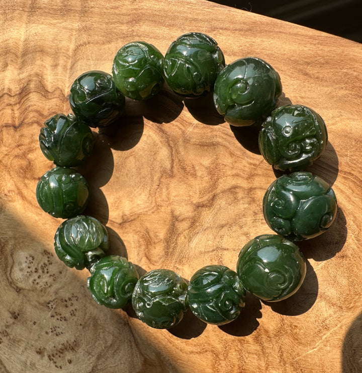 Nephrite jade beads 16mm carved with spiral motifs arranged as a bracelet on a wood surface