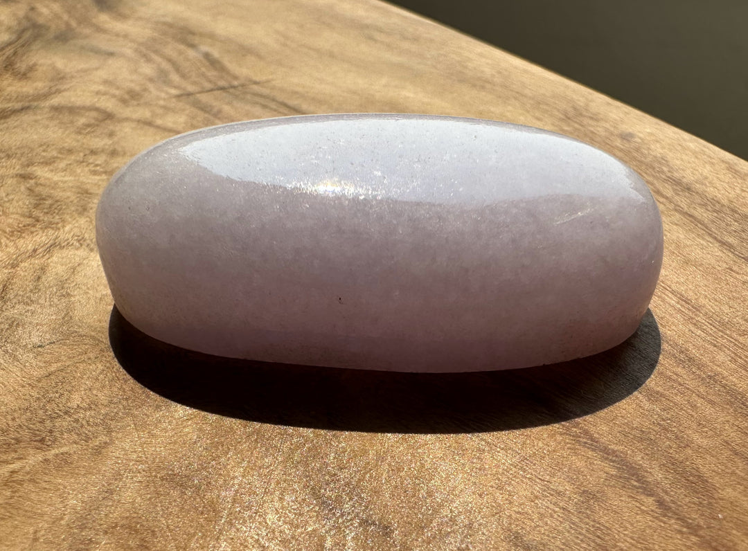 A smooth, polished oval-shaped pale pink stone, resting on a textured wooden surface.