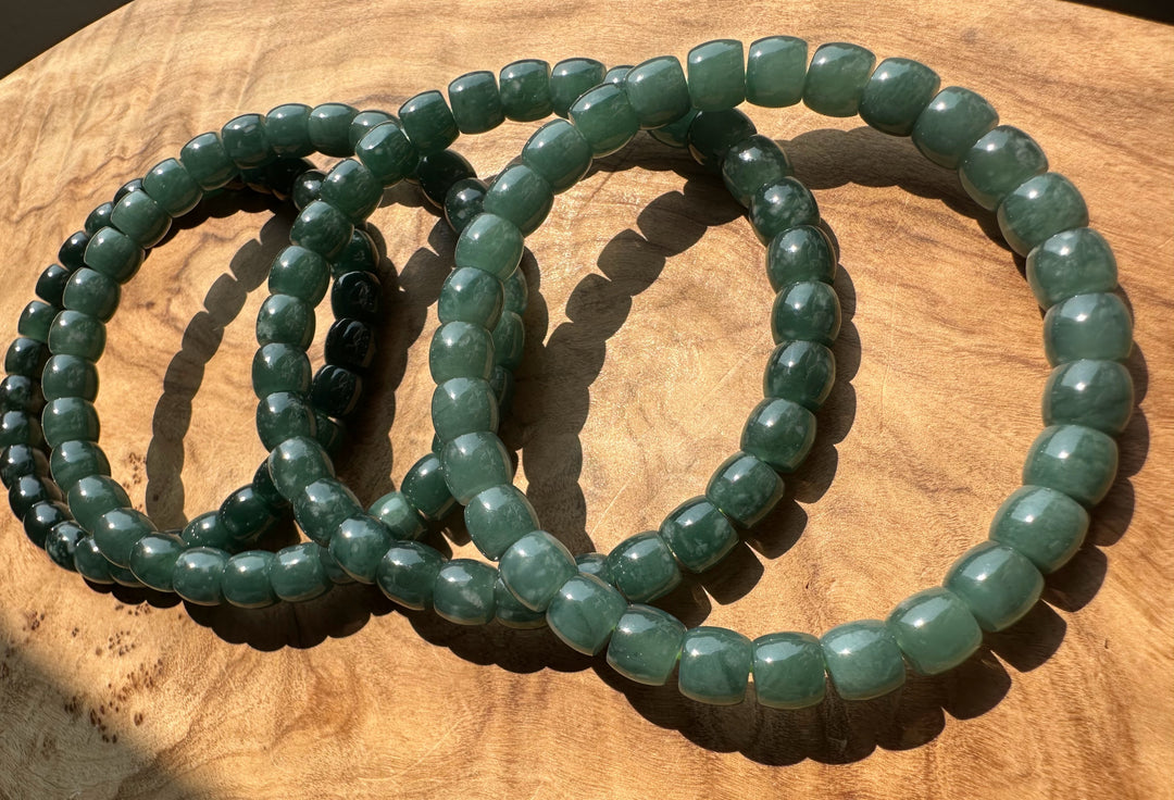 Three green beaded stretch bracelets arranged in overlapping circles on a wooden surface.