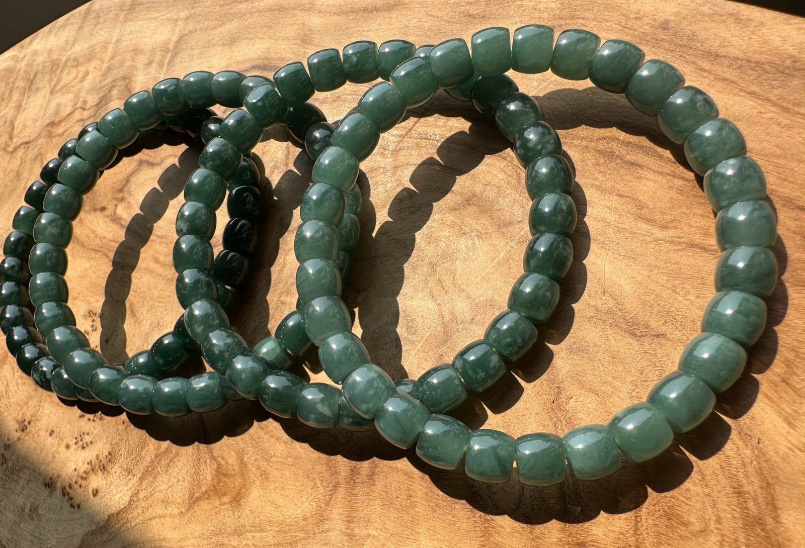 Three green beaded stretch bracelets arranged in overlapping circles on a wooden surface.