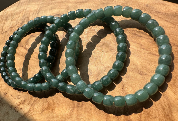 Three green beaded stretch bracelets arranged in overlapping circles on a wooden surface.