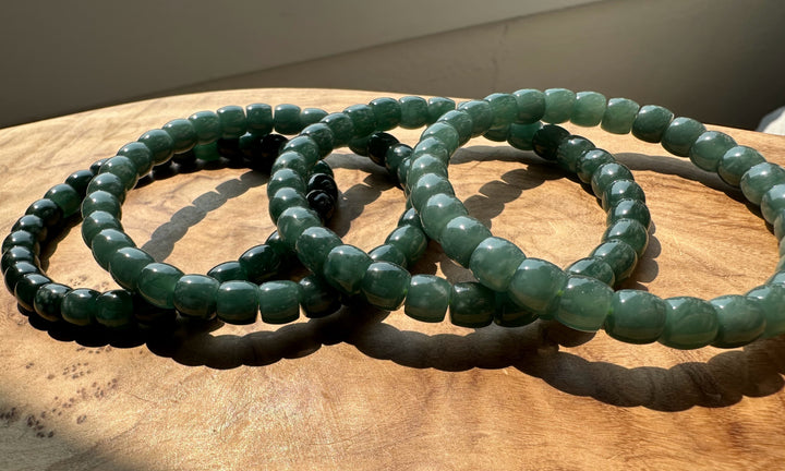 Green beaded stretch bracelets arranged on a wooden surface under warm natural light.