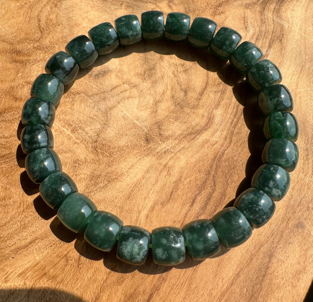 A beaded stretch bracelet made of polished dark green stone beads with natural marbling, displayed on a warm brown wooden surface.